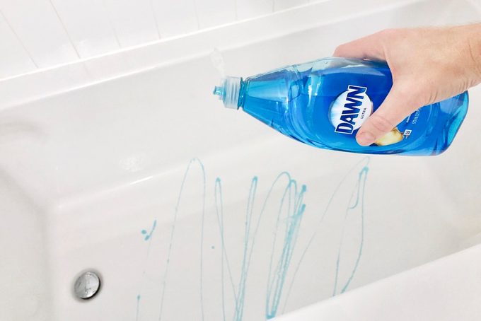 hand holding a bottle of dawn dish soap over a white bathtub pouring some dish soap into the tub