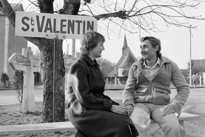 A couple of lovers poses on the occasion of Valentine's Day in Saint Valentin on February 14, 1982. - Young fiancee from Saint Valentin village Michel Leduc 25 years old and Nadia Mouche Bouef 24 years old, wisely wait on a bench of the village the 140 new fiancés of the four corners of France. (Photo by Daniel JANIN / AFP) (Photo credit should read DANIEL JANIN/AFP via Getty Images)