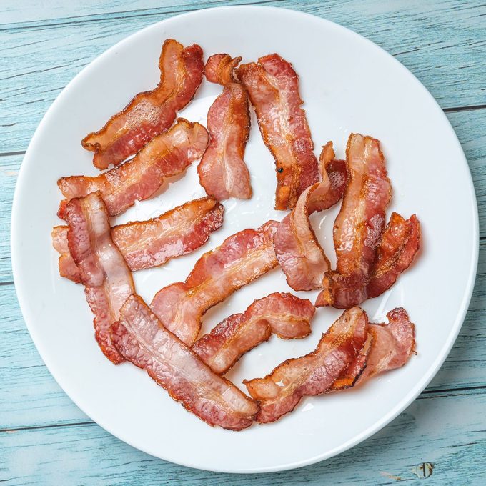 Cooked fired bacon rashers white dish and blue wooden background, Morning Breakfast Concept, View from Top, Flat Lay
