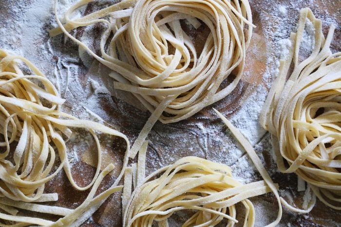 Close-up image of homemade tagliatelle nest pasta dough dusted in flour and left to dry on floured wooden chopping board, Italian cuisine elevated view