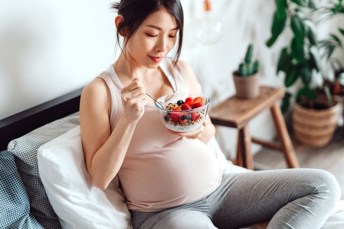 pregnant woman eating healthy breakfast in bed