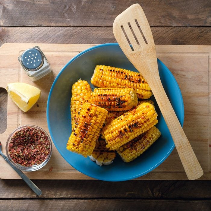 Yellow corn cobs, sprinkled with spices on a bright ceramic plate, against the background of a wooden table. The concept of cooking homemade food. Vegetarian and vegan food, diet. Organic farm products.