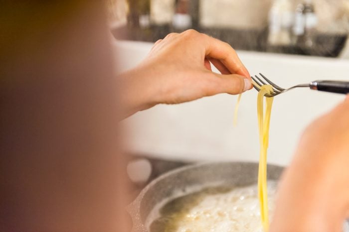Woman preparing spaghetti, trying if they are ready to eat