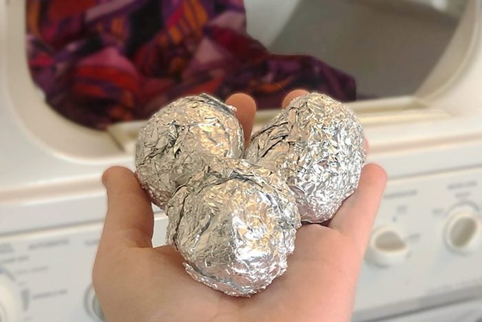 hand holding three rolled tin foil balls in front of dryer