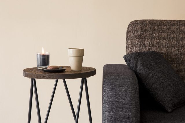 Detail view of modern round wood metal coffee table with cappuccino mug, glass candle burning by the side of sofa.