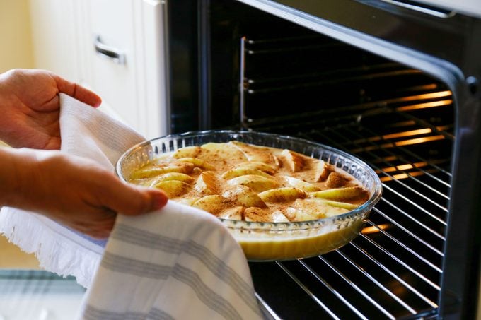 person placing a tart in a glass dish into an open oven