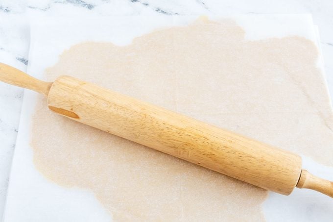 Tagalongs dough rolled out between sheets of parchment paper; a rolling pin sits on top