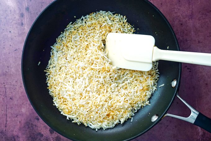 toasting the shredding coconut in a pan on purple background