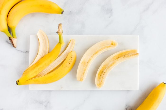 Bananas on White Marble Board; one banana has been peeled and cut in half the lengthwise
