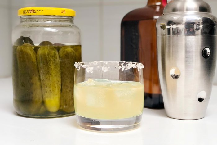pickle juice margarita in a glass next to a jar of pickles and a cocktail shaker