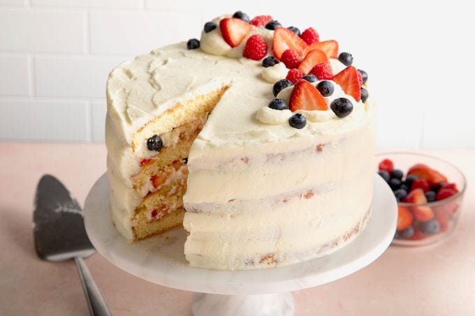 finished layered berry Chantilly cake on a cake stand with a slice taken out