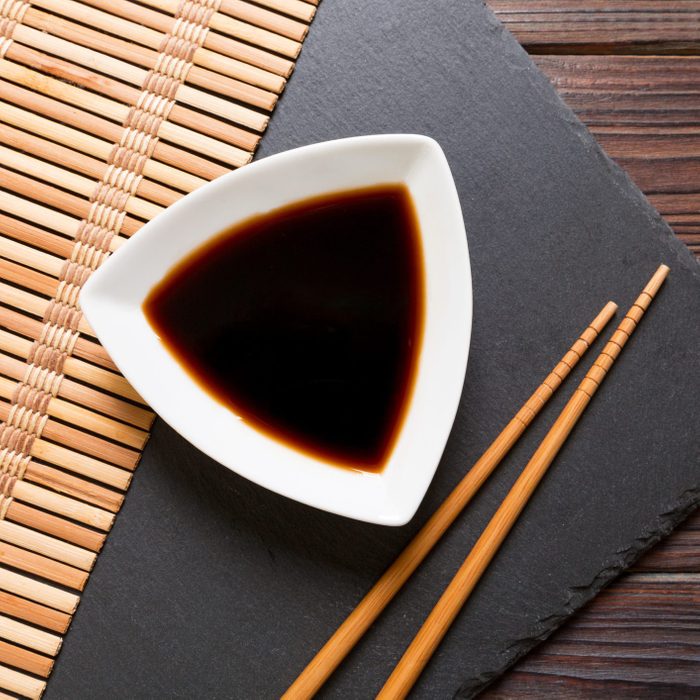 Chopsticks and soy sauce on black stone plate, wooden background with copy space