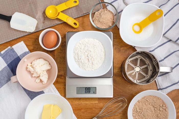 measuring Flour on digital scale with other ingredients surrounding with measuring cups and spoons