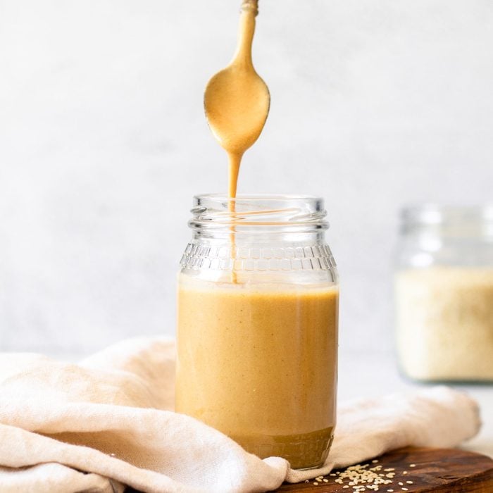 Cropped hand of woman lifting spoon of tahini out of jar