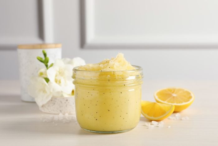 Body scrub in glass jar, freesia flowers and lemon on wooden table