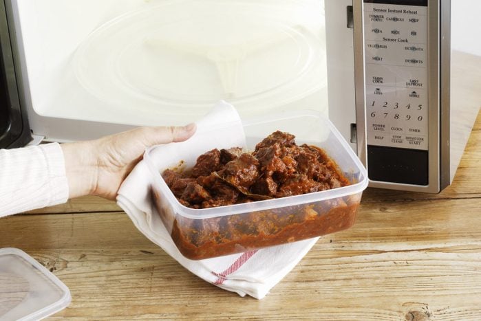 Woman heating plastic container of leftovers in a microwave