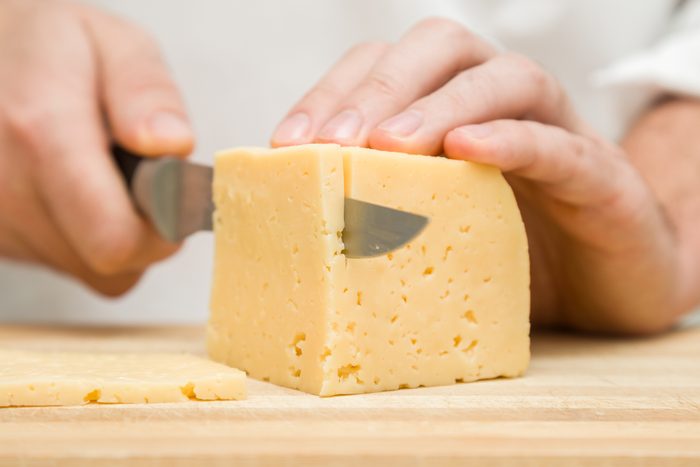 Chef's hands with knife cutting a cheese on the wooden board