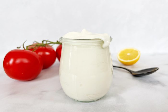 Jar of homemade vegan mayonnaise with tomatoes and lemon in the background