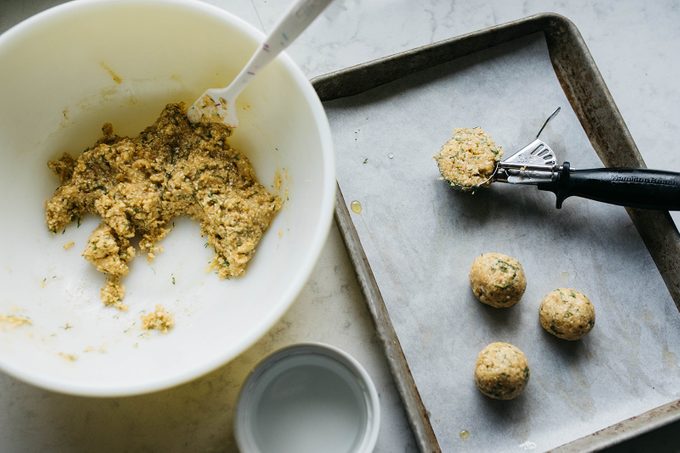 a bowl with matzo batter next to a cookie sheet with an ice cream scoop for shaping into balls