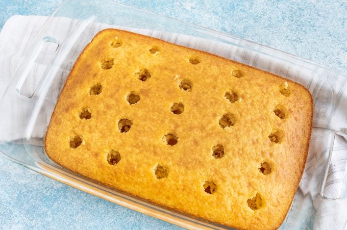 yellow cake in a rectangular glass pan with unorganized grid of holes poked top