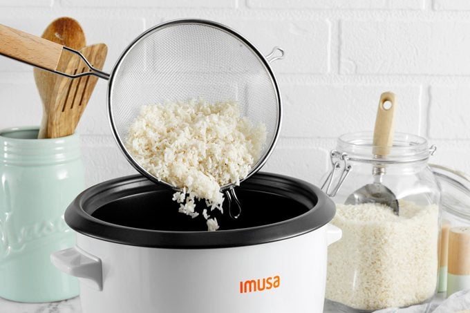 dumping uncooked white rice into a rice cooker