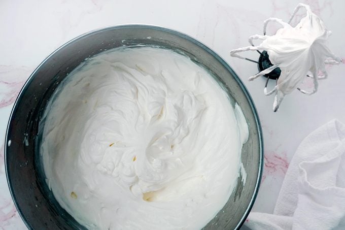 Homemade whipped cream in a bowl on a white marble kitchen counter, view from above