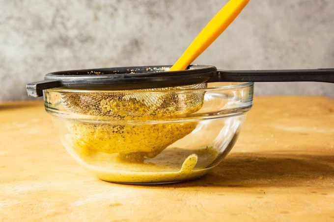 making smooth dijon mustard with a strainer and a glass bowl