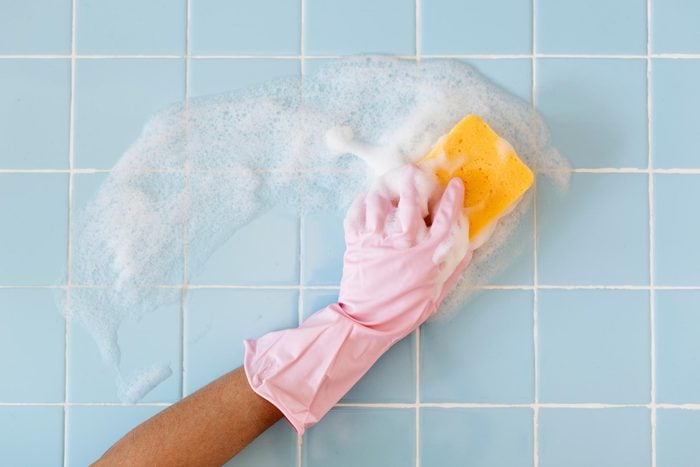 Hand in pink glove with sponge washing blue bathroom tiles