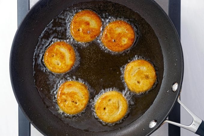 potato smileys arranged in a circle in a small frying pan with hot oil, view from above