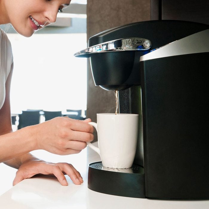 close up of a woman filling a white coffee mug with coffee using a Keurig
