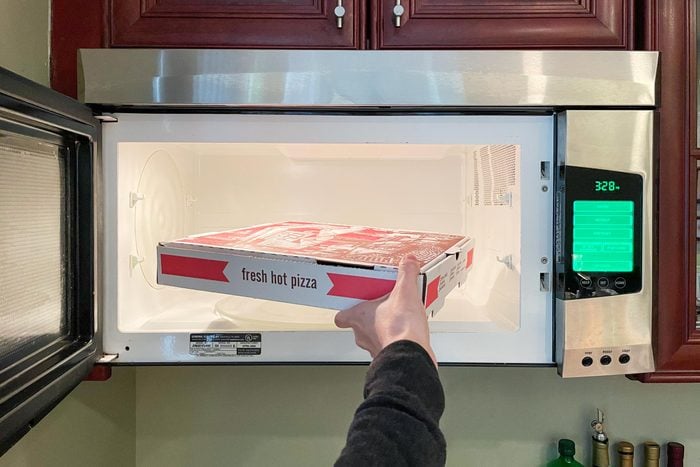 hand putting a cardboard pizza box into an open microwave