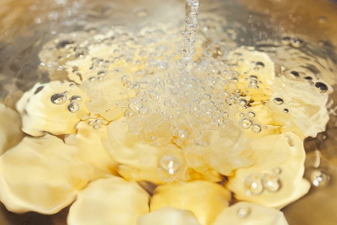 Raw, peeled potatoes under cold running water in chrome bowl in the sink