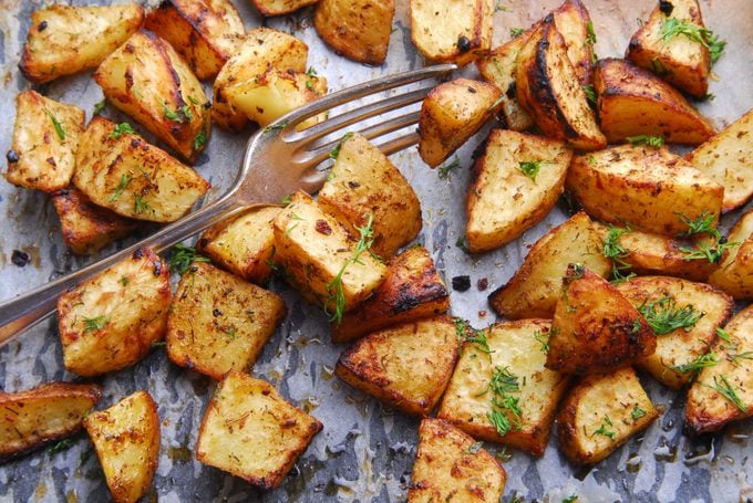close up of oven roasted potatoes on a baking sheet garnished with herbs