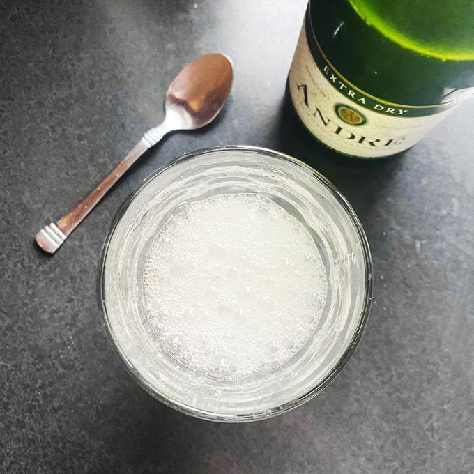 cup of bubbly champagne on a counter with the bottle and a spoon
