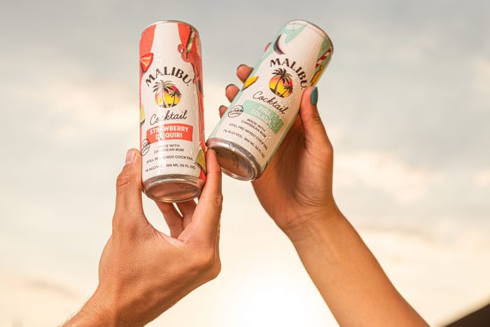hands with Malibu canned cocktails against a sunset