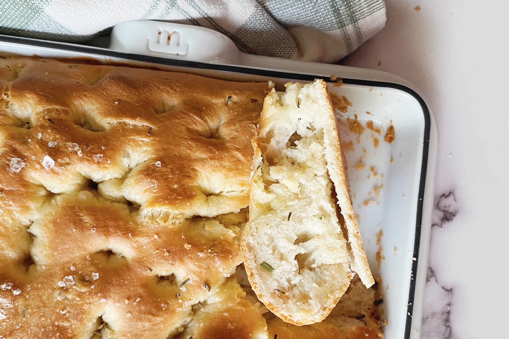 baked focaccia with a piece taken out in a madeinslab pan on a kitchen counter top