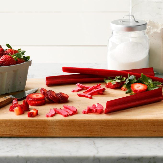 Rhubarb And Strawberries chopped and sliced on a wooden cutting board on a marble kitchen counter