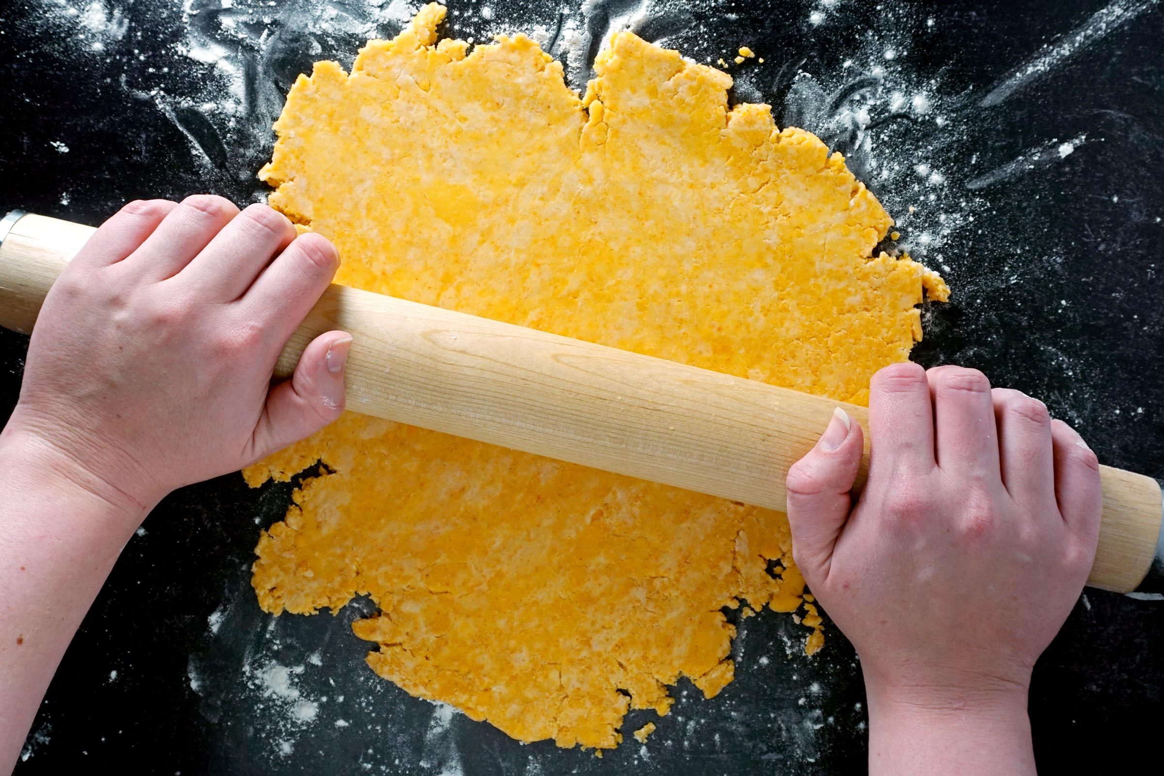 hands using a rolling pin to roll out dough for Homemade Cheez Its