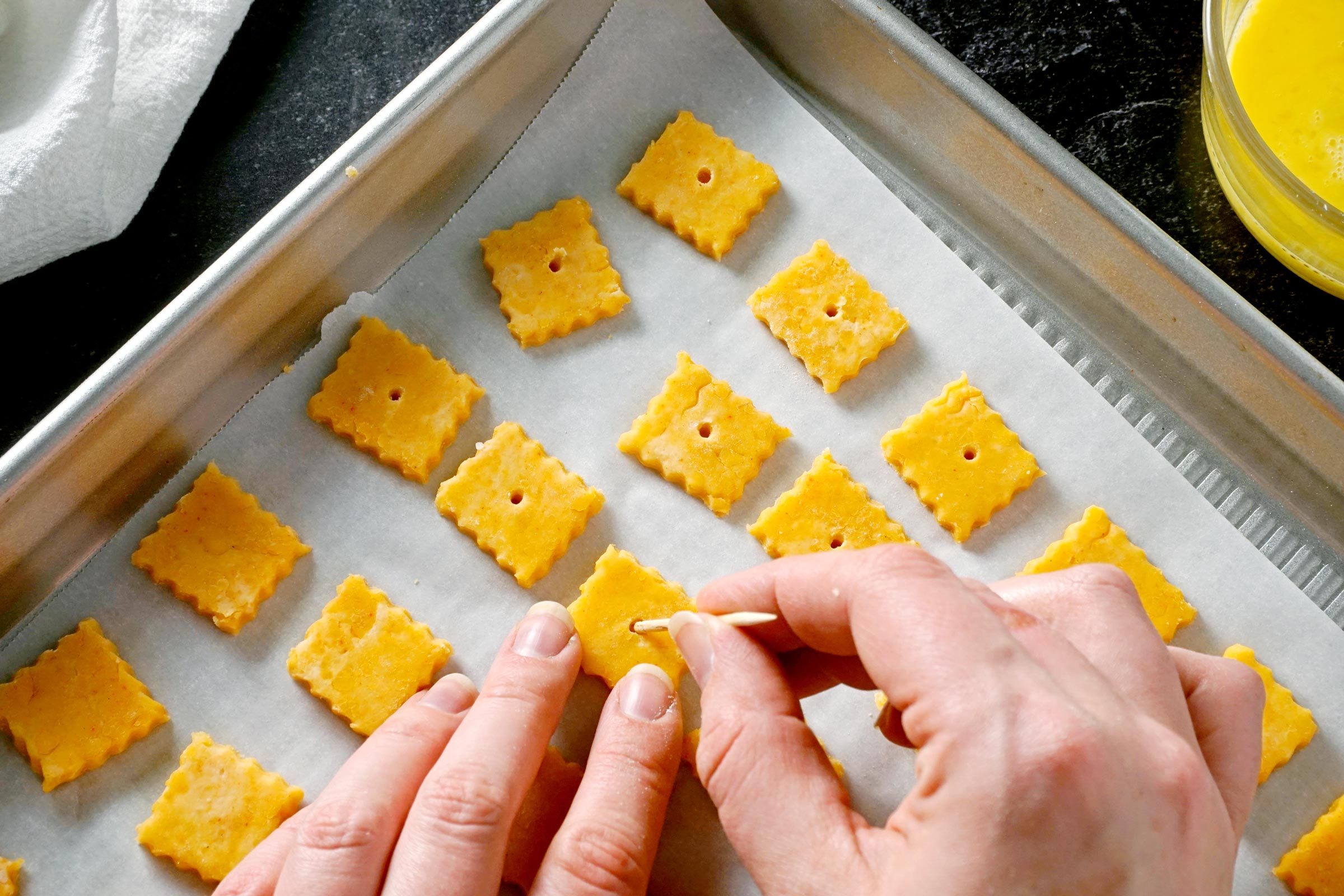 hands using a tooth pick to shape Homemade Cheez Its on a baking sheet ready to bake