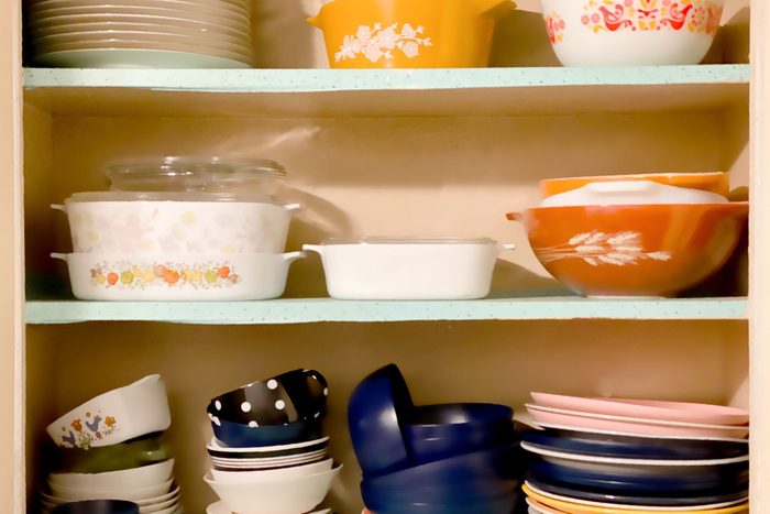 vintage 1950s white wall kitchen cabinets open revealing shelves of old-fashioned Pyrex kitchenware