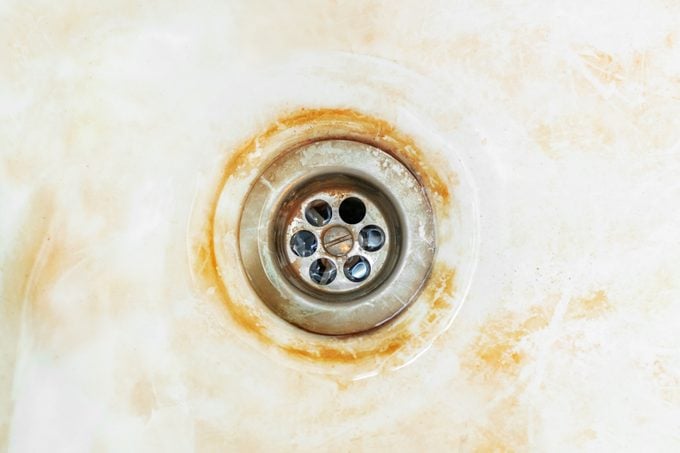 Old rusty bathtub with a metal drain hole. Dirty cracked unclean surface of the bath or sink with red rust stain, close-up. Corrosion, unsanitary.