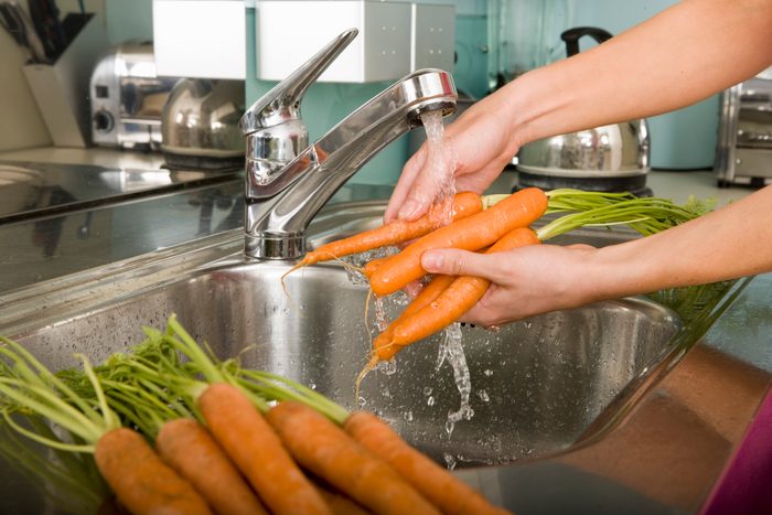 Woman washing carrots at kitchen sink, close-up