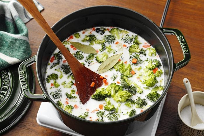 adding veggies and stock to the pot for cheesy broccoli soup