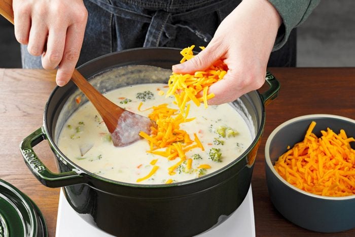 thickening soup by adding cheese to a pan for Cheesy Broccoli Soup