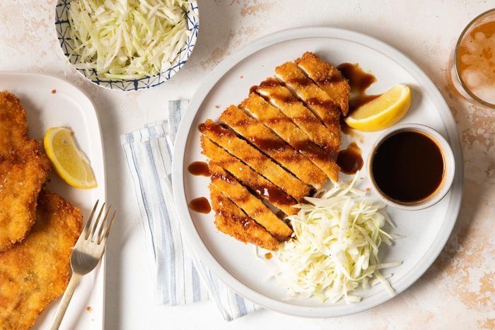 A Plate of Chicken Katsu With Sliced Cabbage, Sauce and Lemon Slices