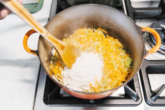 adding flour to the vegetables in the pot to make a roux