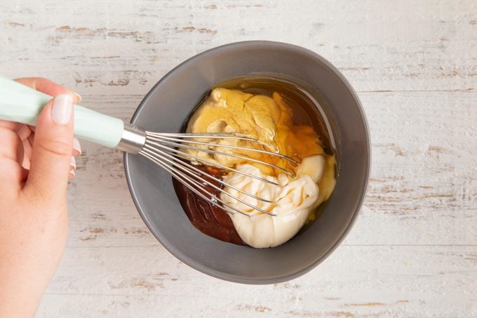 multiple ingredients for making chick fil a sauce in bowl with a whisk