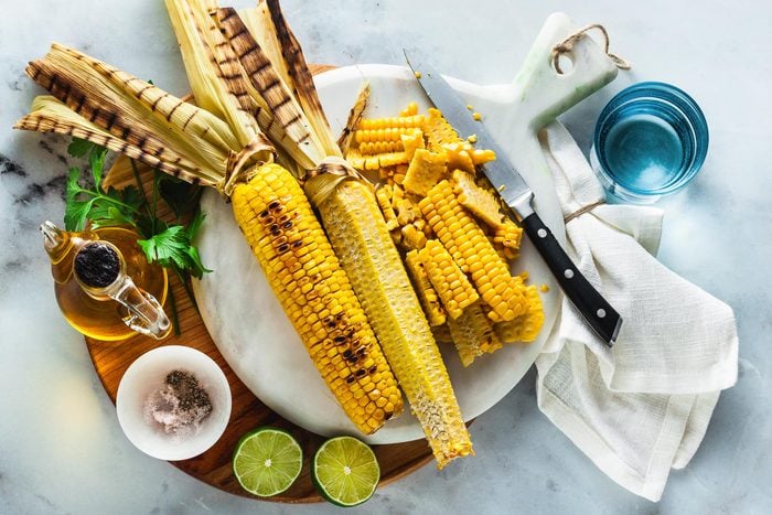 ears of corn and corn cut off the cob on a cutting board on a white stone kitchen counter