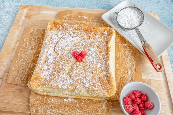 baked Magic Cake on a cutting board topped with powdered sugar and raspberries