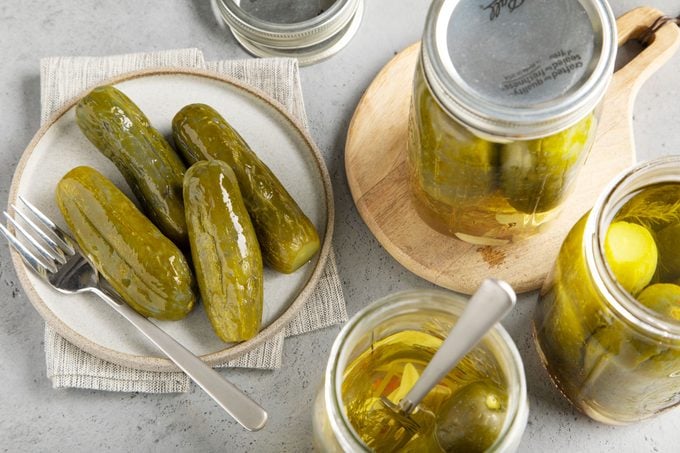 homemade whole cucumber pickles on a plate next to jars of pickles